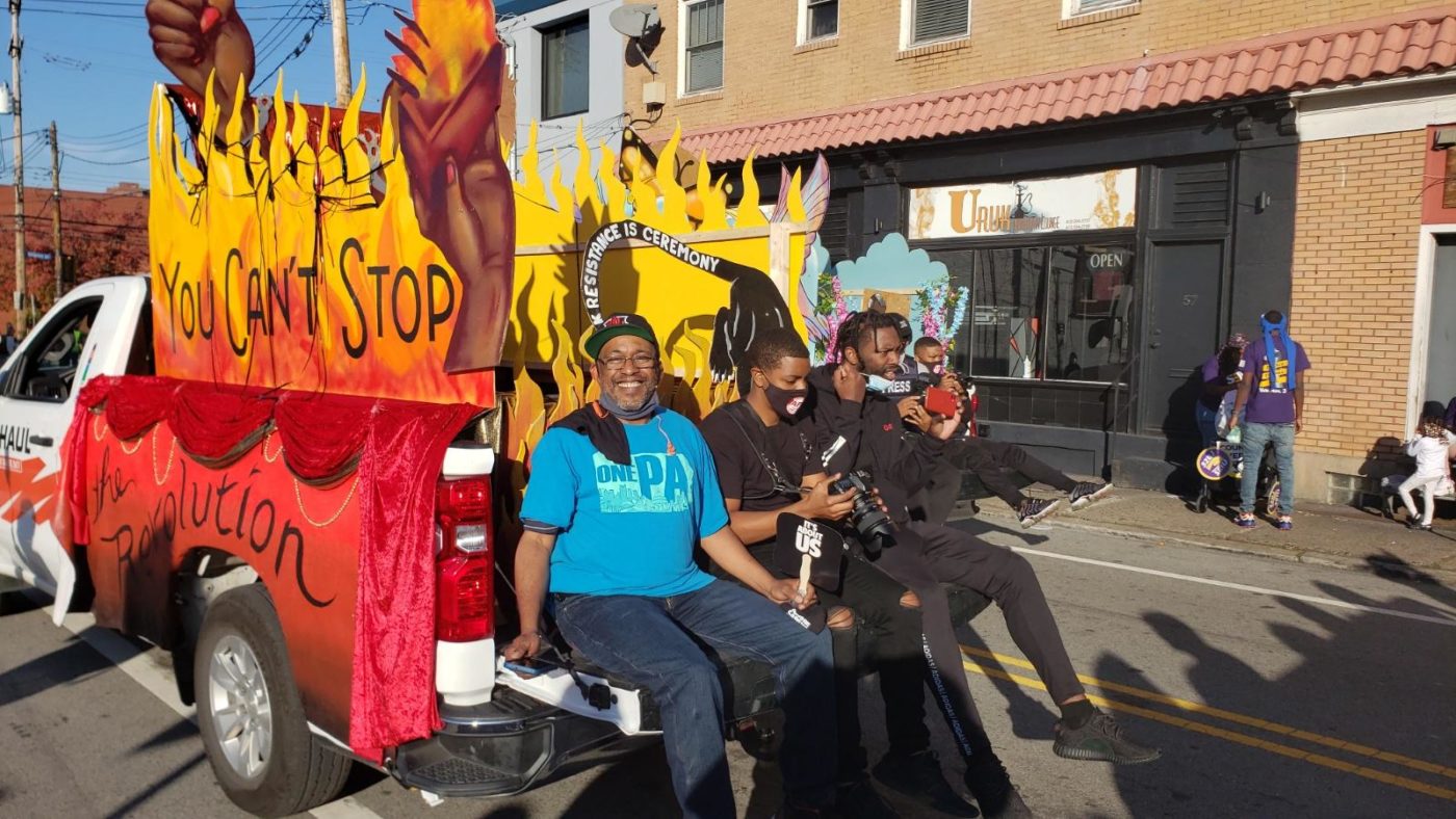 men riding in the back of a truck decorated with art that says you can't stop the revolution