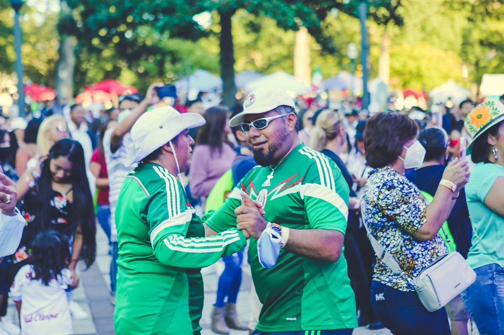 ALForward CASE STUDY IMAGE 2_ Two masc presenting people in green soccer jerseys dance at a cultural festival (1) (1)