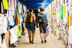 two people walking down a hall with posters on the walls