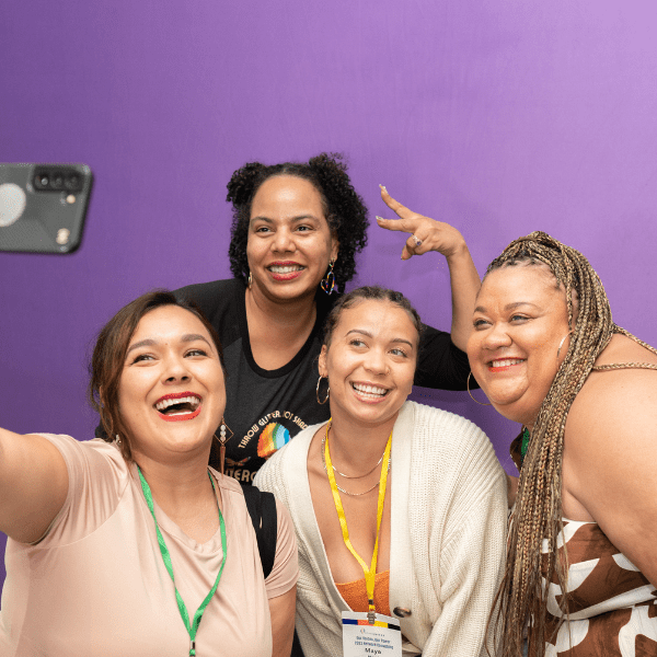 Members from State Voices leadership including Alexis Anderson Reed and Maya Neal, pose for a selfie photo in front of a lavender background