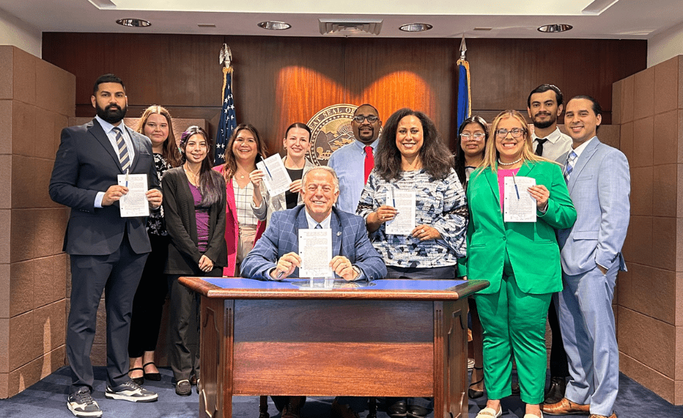 Nevada advocates, including Silver State Voices Executive Director Emily Zamora, stand with Assemblywoman Brittney Miller behind a seated Governor Joe Lombardo for the signing of bill #AB286.