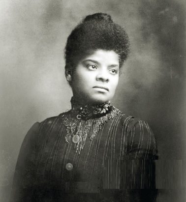 Archival black and white photo of trailblazing African American journalist and organizer, Ida B. Wells-Barnett. Wells-Barnett is a 20th century Black woman wearing a ruffled dress. Her hair is styled in an updo.
